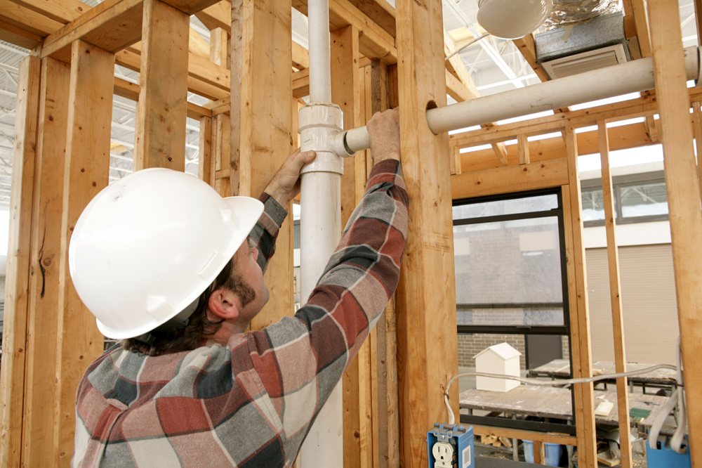 Technician in a hard hat installing PVC plumbing in new construction wall framing